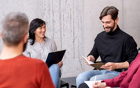 Gruppe mit jungen Menschen arbeiten gut gelaunt in einem Stuhlkreis zusammen.